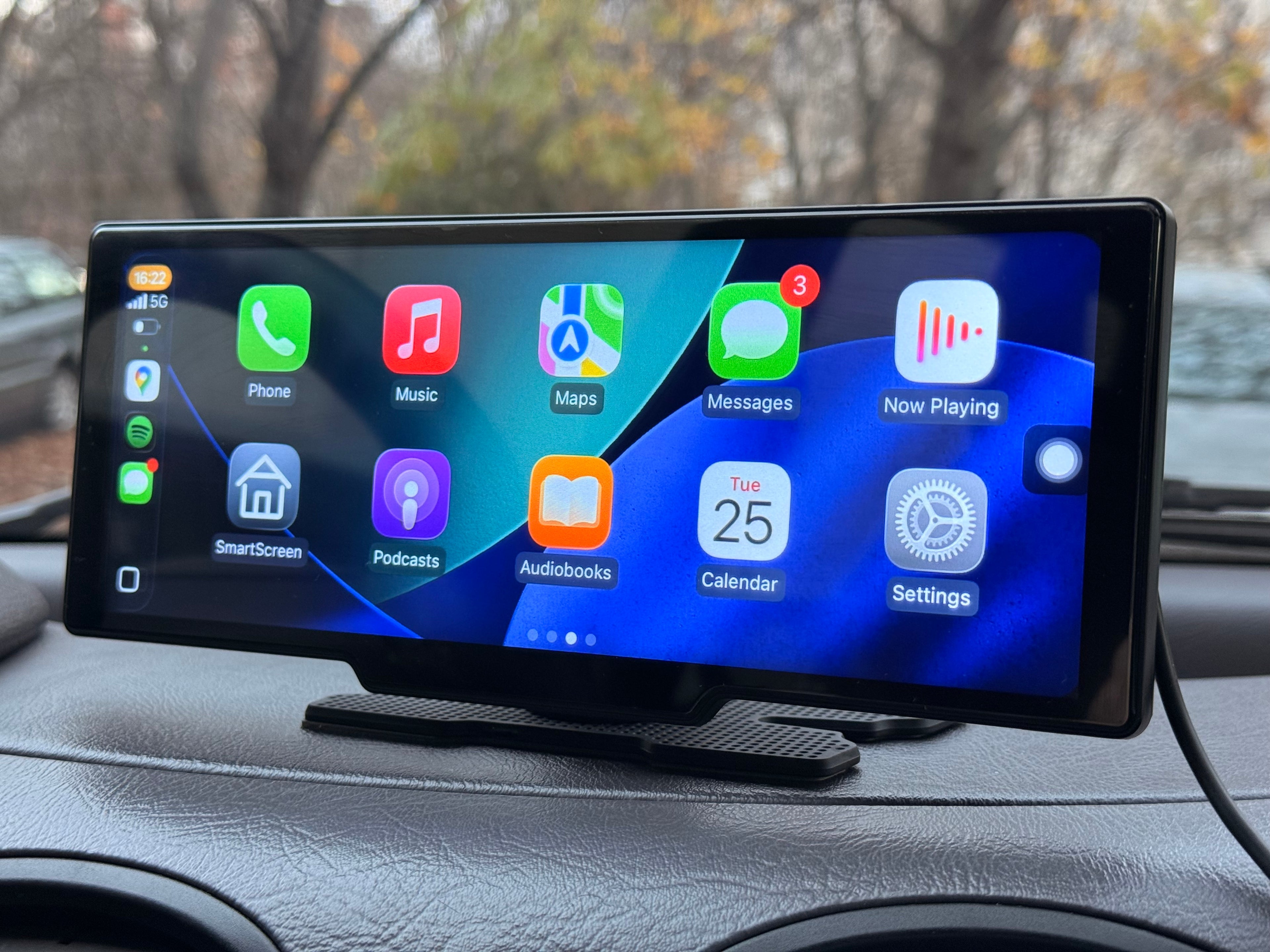 Поставен в автомобил външен дисплей, показващ интерфейс на CarPlay с икони за Phone, Music, Maps, Messages и други приложения.